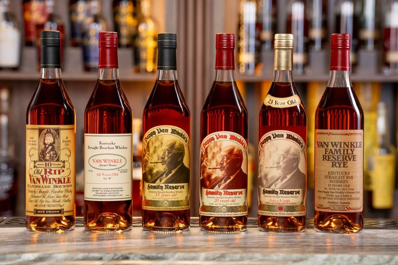 A row of rare Van Winkle and Pappy Van Winkle bourbon bottles lined up on a warm, backlit bar